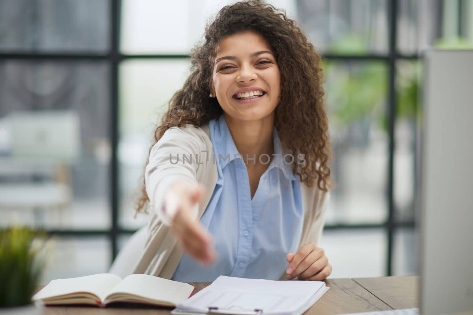 Happy young woman looking at the camera while welcoming a client. Smiling female executive manager, secretary offering professional business services