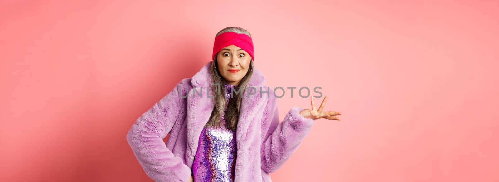 Fashion and shopping concept. Confused senior hipster woman looking puzzled, shrugging with hand spread sideways and clueless stare, standing over pink background.