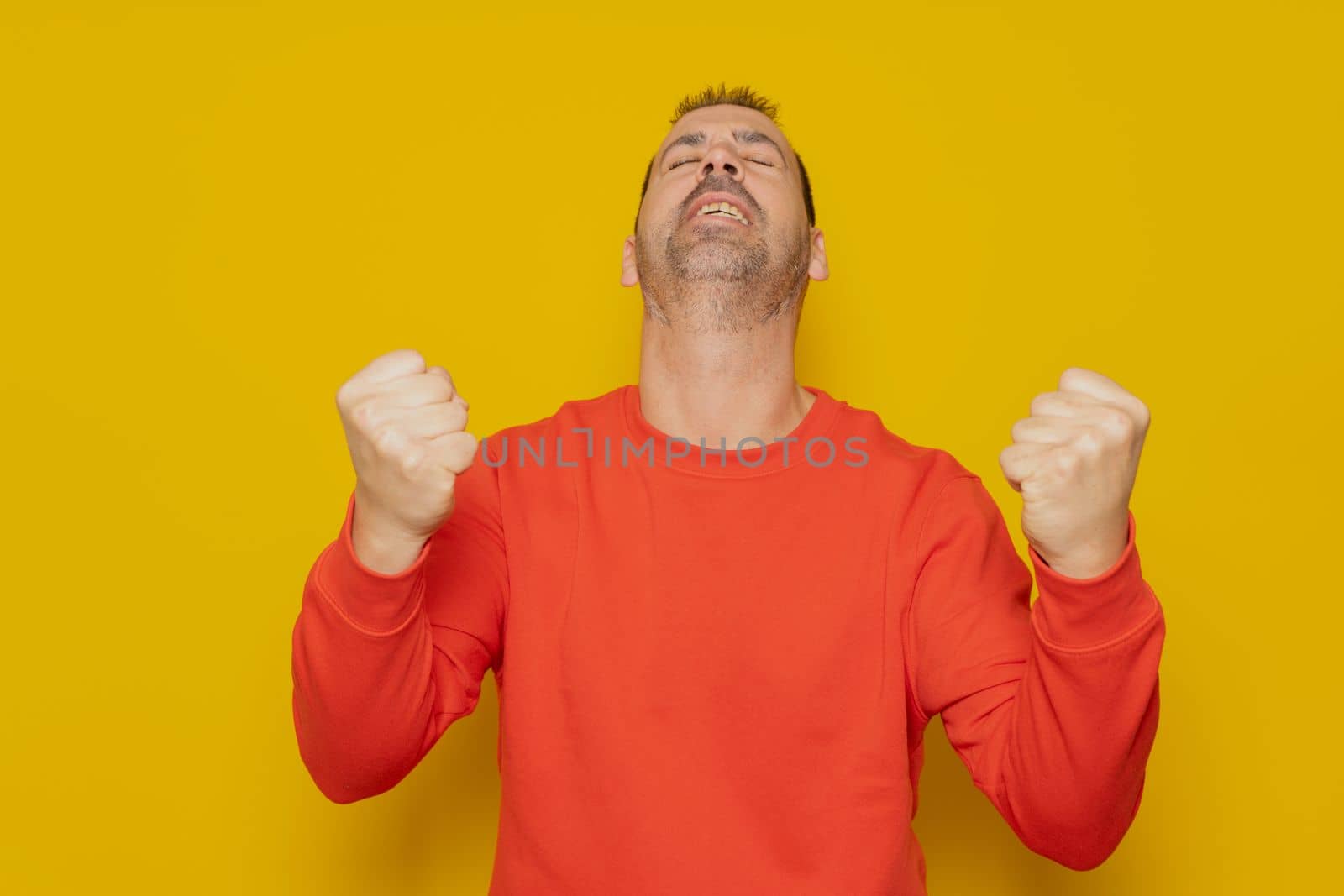 Portrait of a satisfied man celebrating success with raised fists and looking up isolated over yellow background.