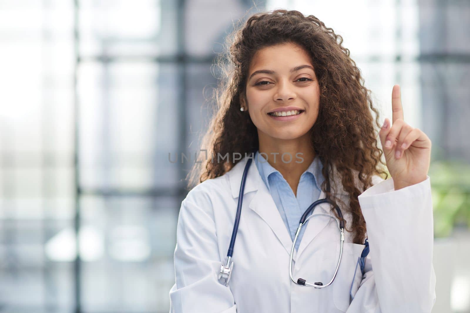 Portrait of an attractive young female doctor in a white coat points her finger