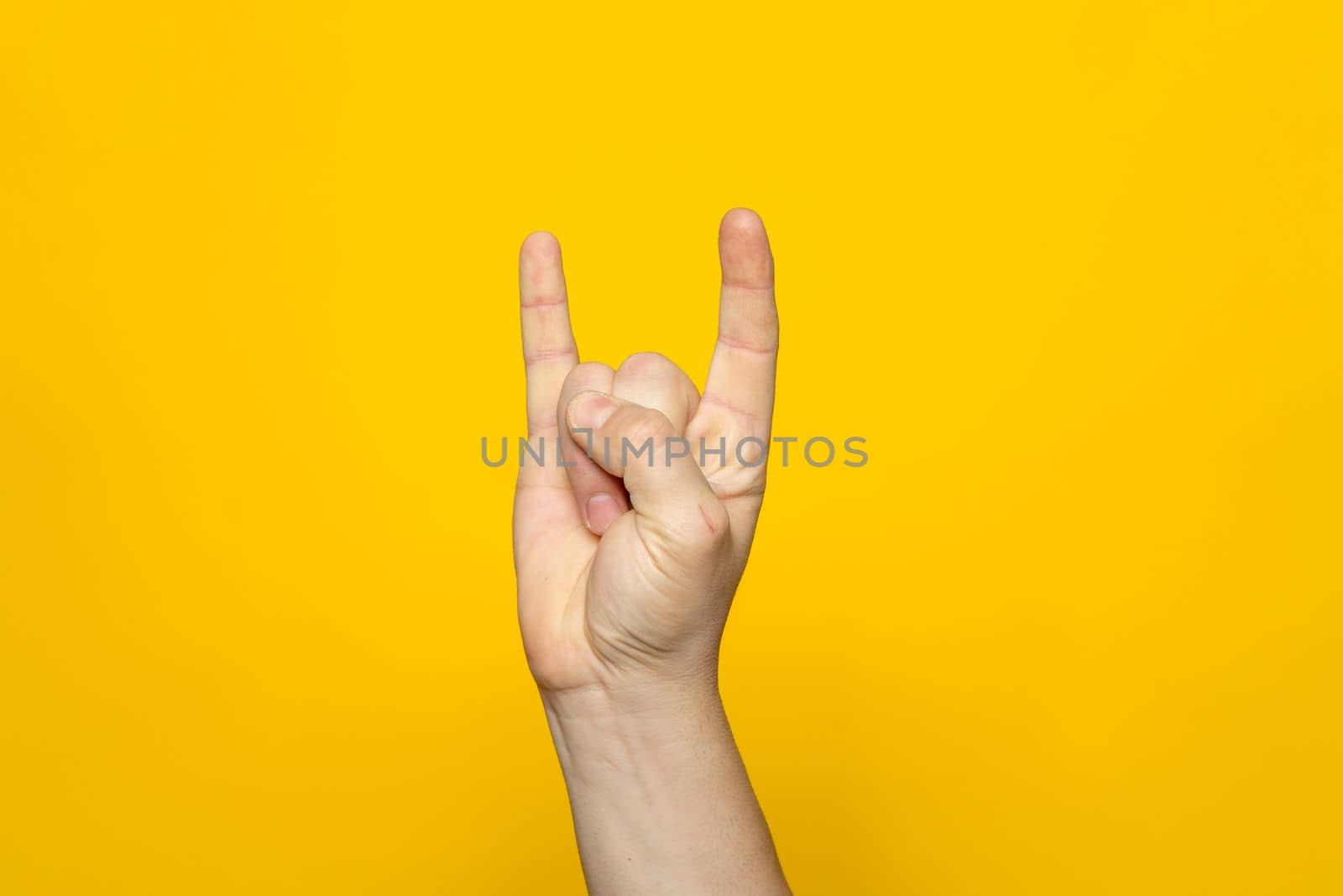 Strong hand of man making the rock gesture on a yellow studio background