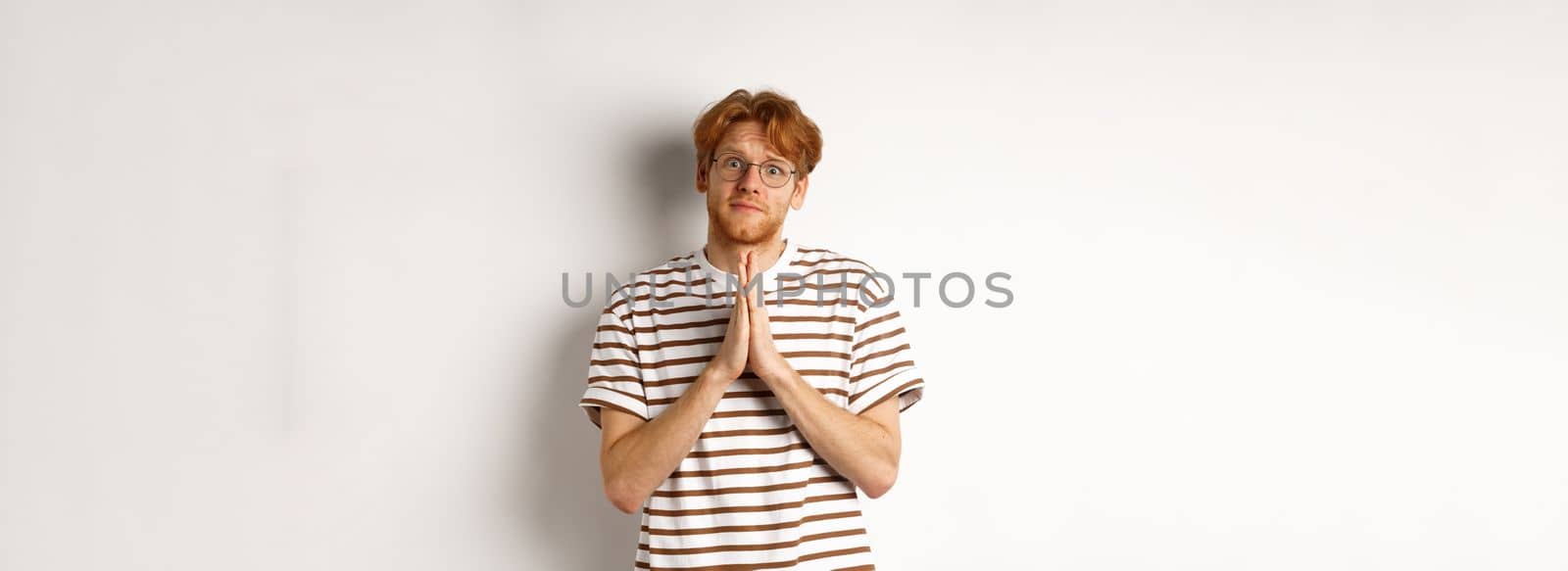 Cute redhead man in glasses asking for help, pleading and looking clingy at camera, begging for favour, white background.