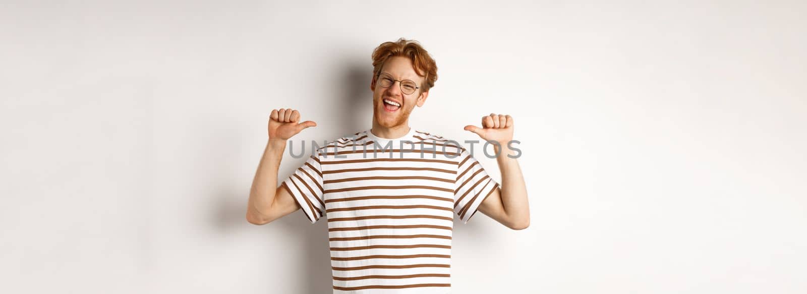 Cheerful and funny redhead man with beard, wearing glasses, laughing and pointing at himself, standing over white background by Benzoix