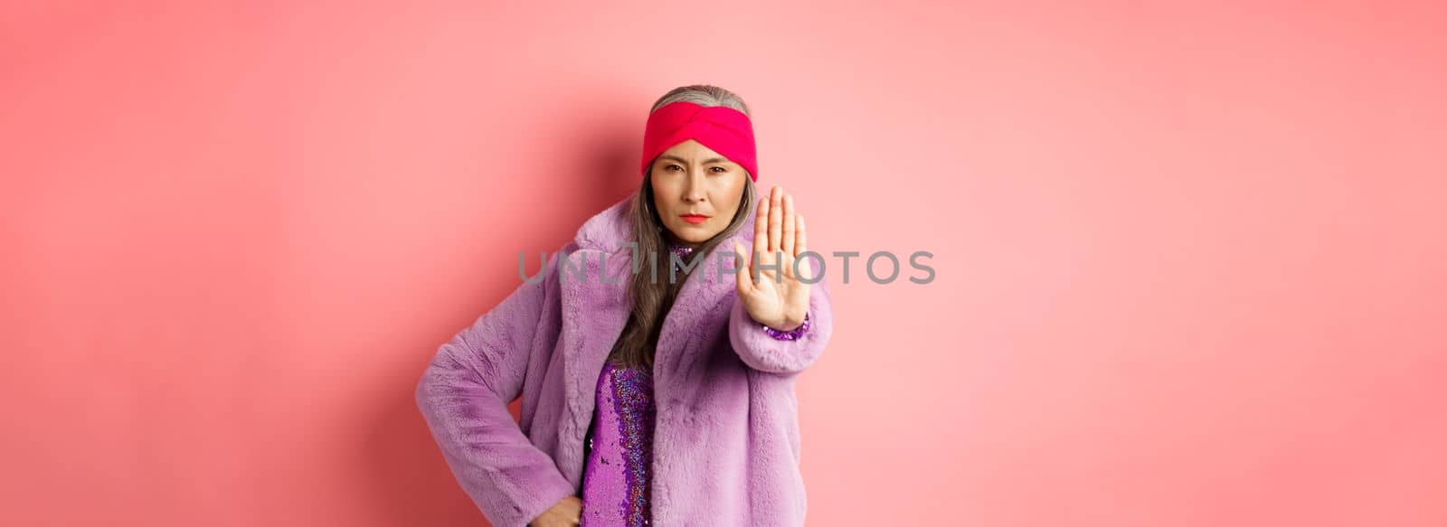 Fashion and shopping concept. Serious asian senior woman showing stop sign to warn and prohibit something, looking determined at camera, wearing stylish purple clothes.