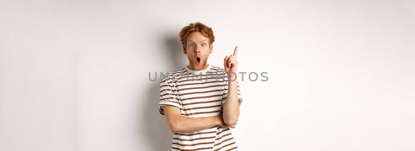 Excited redhead man having revalation, raising finger in eureka sign and saying idea, standing over white background.