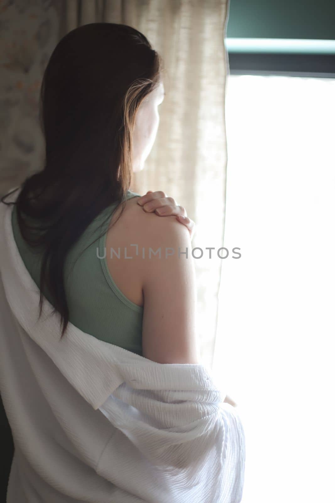 Beautiful woman in white silk pyjama standing near window in a cozy room. emotional portrait.