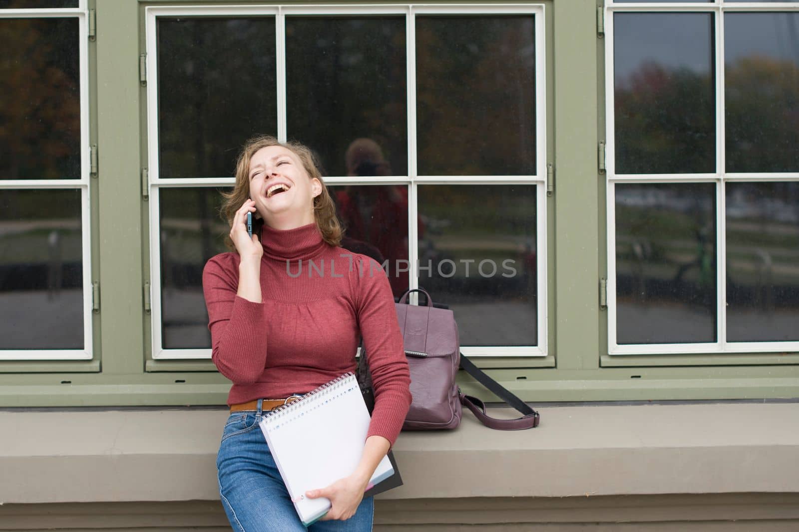 a young caucasian girl returns to college, stands with a backpack and notebooks and talks on the phone in a laugh, back to school, High quality photo