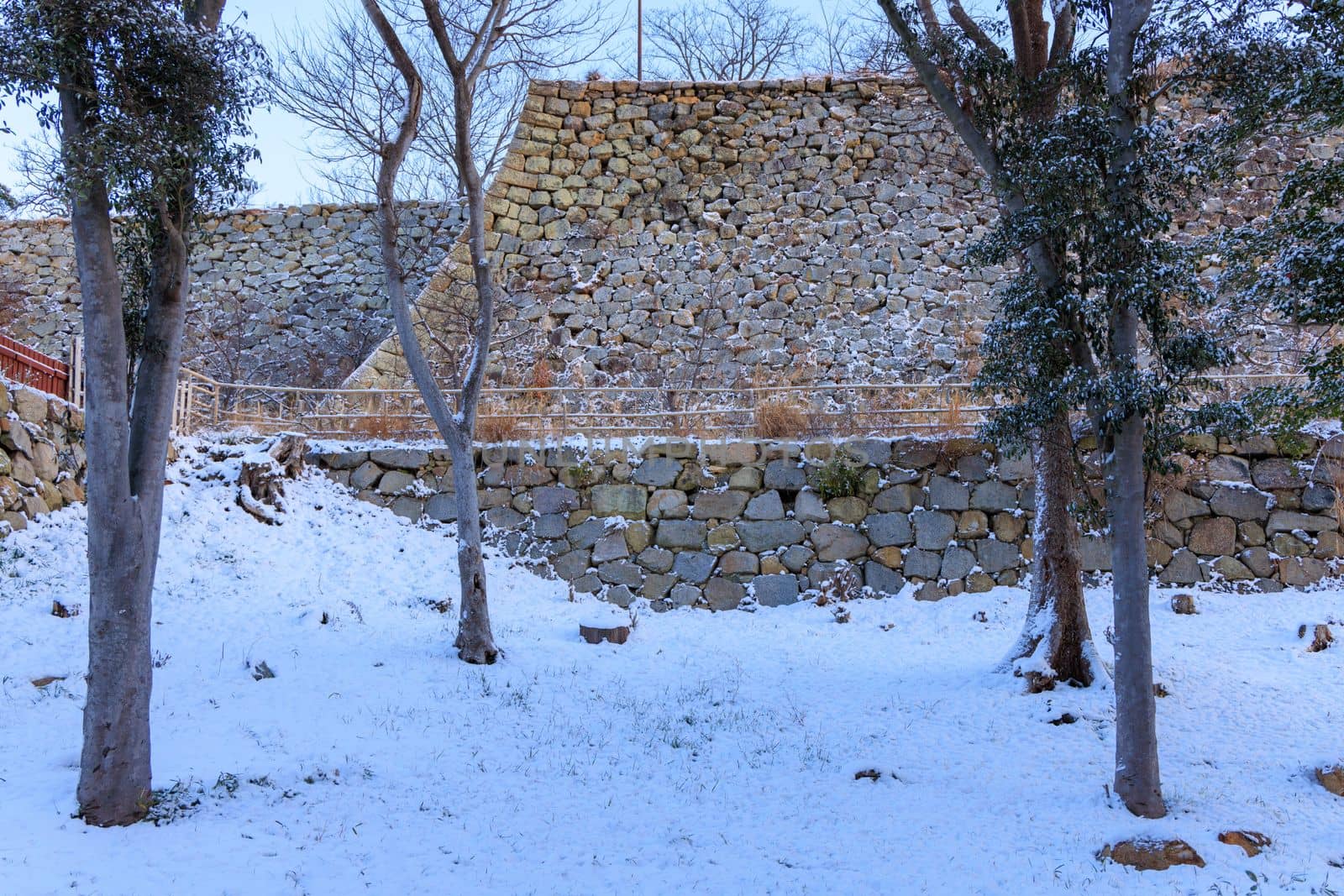 Ancient stone castle wall towers over trees and snow on winter day. High quality photo