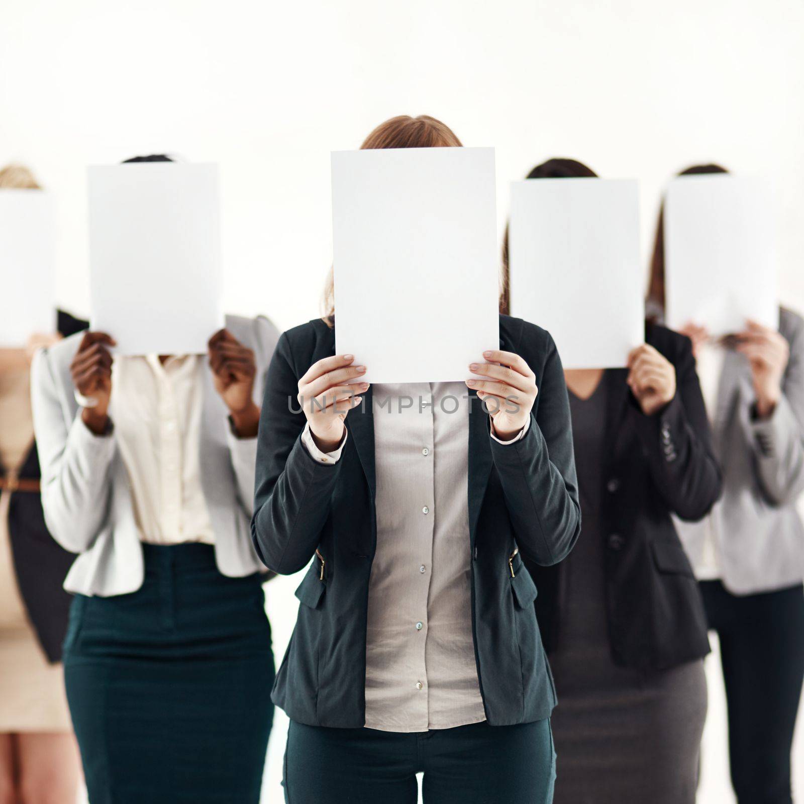 The women behind the business. a group of unrecognizable businesspeople holding blank pieces of paper over their faces against a white background. by YuriArcurs