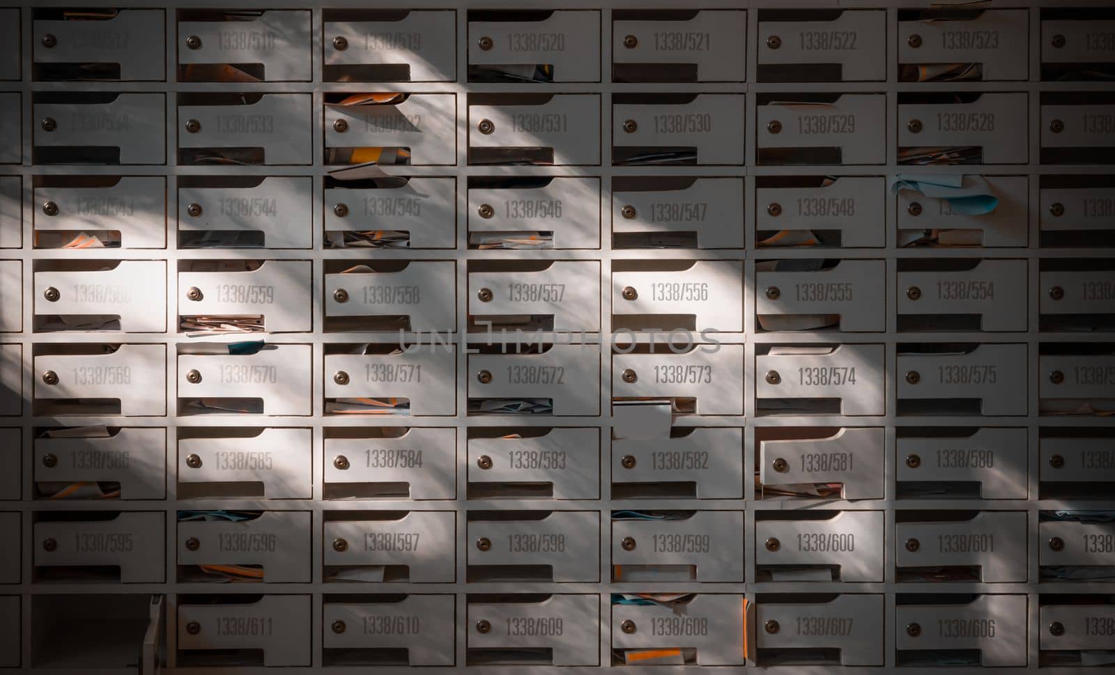 Bangkok, Thailand - 28 Jan, 2023 - Beautiful sunlight shine on rows of white wooden mailboxes with keyholes for resident in condominium or apartment. Postbox in condo, Light and shadow, Selective focus.