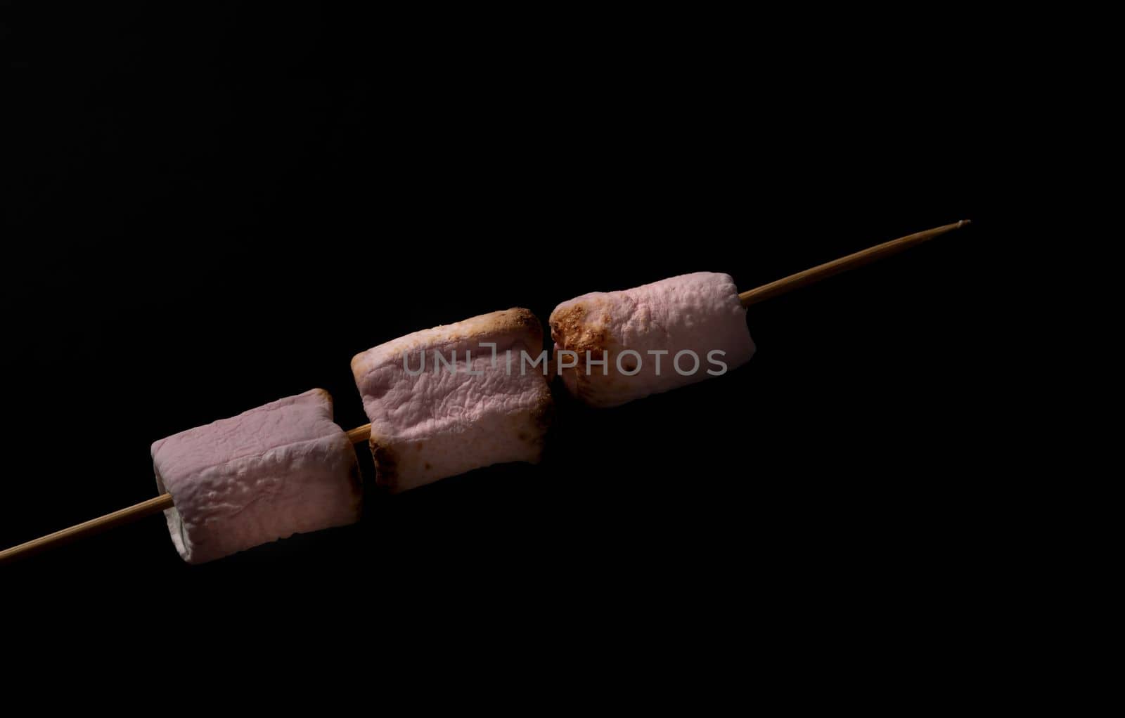skewer of sweet marshmallows warming in the fire on a black background
