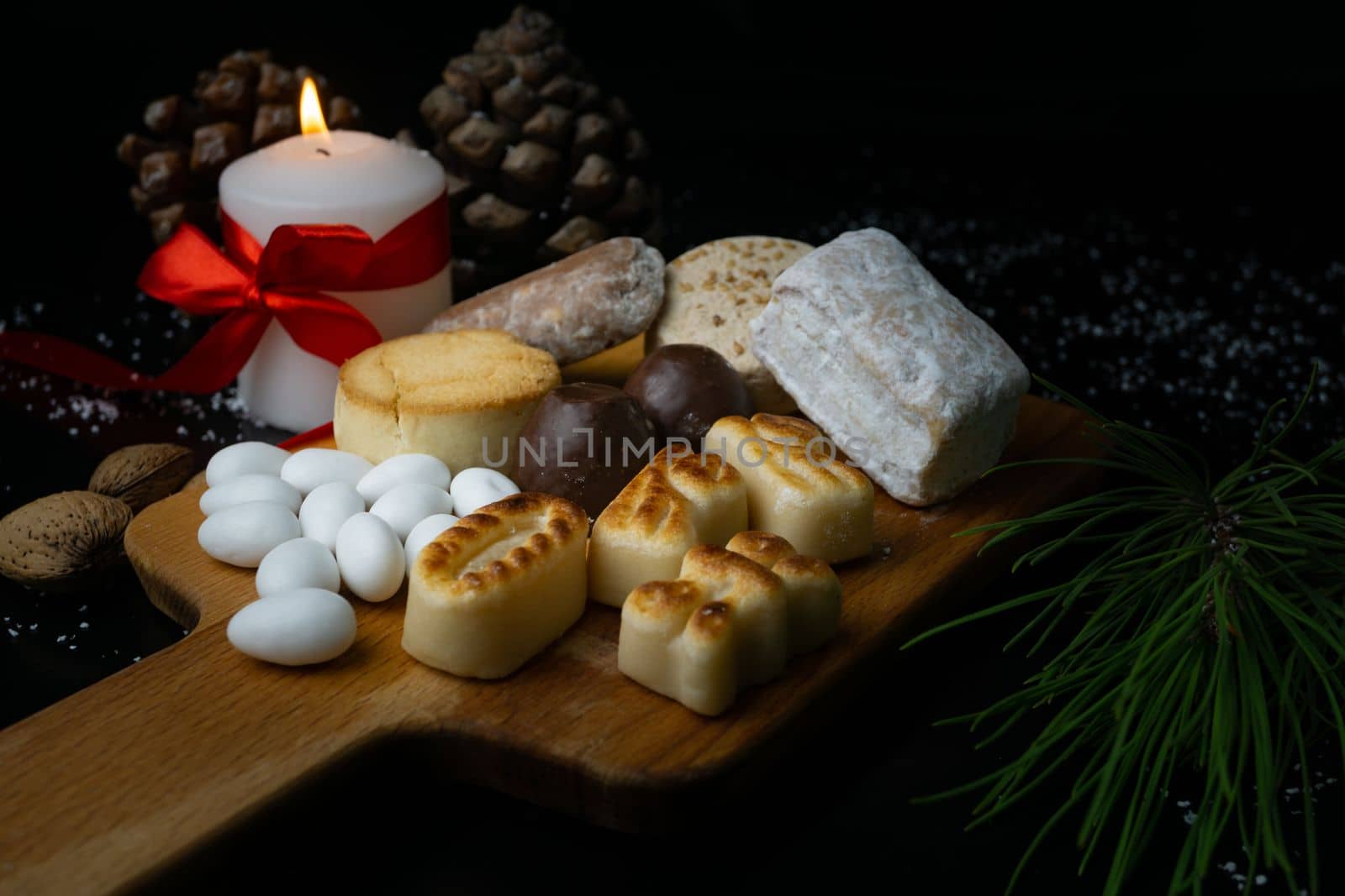 typical christmas sweets on the table decorated with pine cones, pine branches and coloured candles.