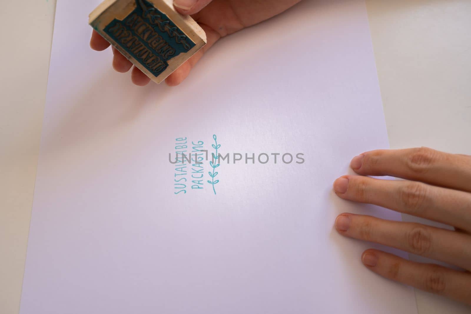 woman's hands placing a sustainable packaging stamp on a blank sheet of paper