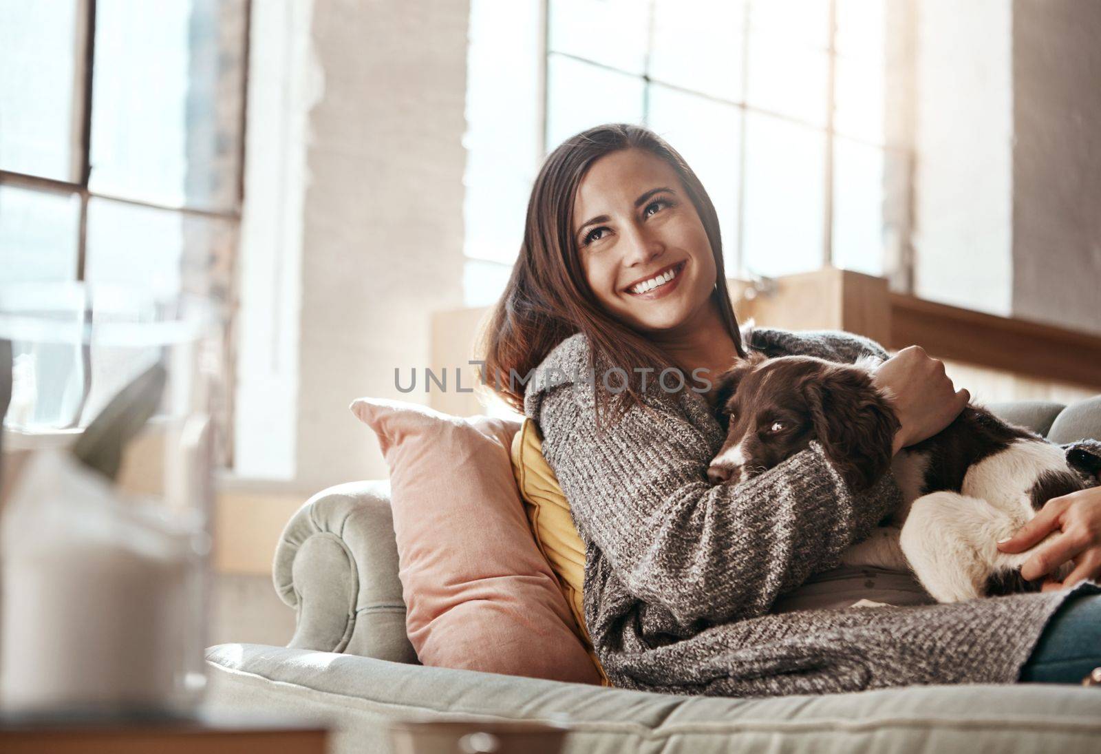 Woman relax on couch with dog, smile and content at home with pet and happy together with peace in living room. Happiness, love for animals and care with female and puppy, cuddle on sofa in apartment.
