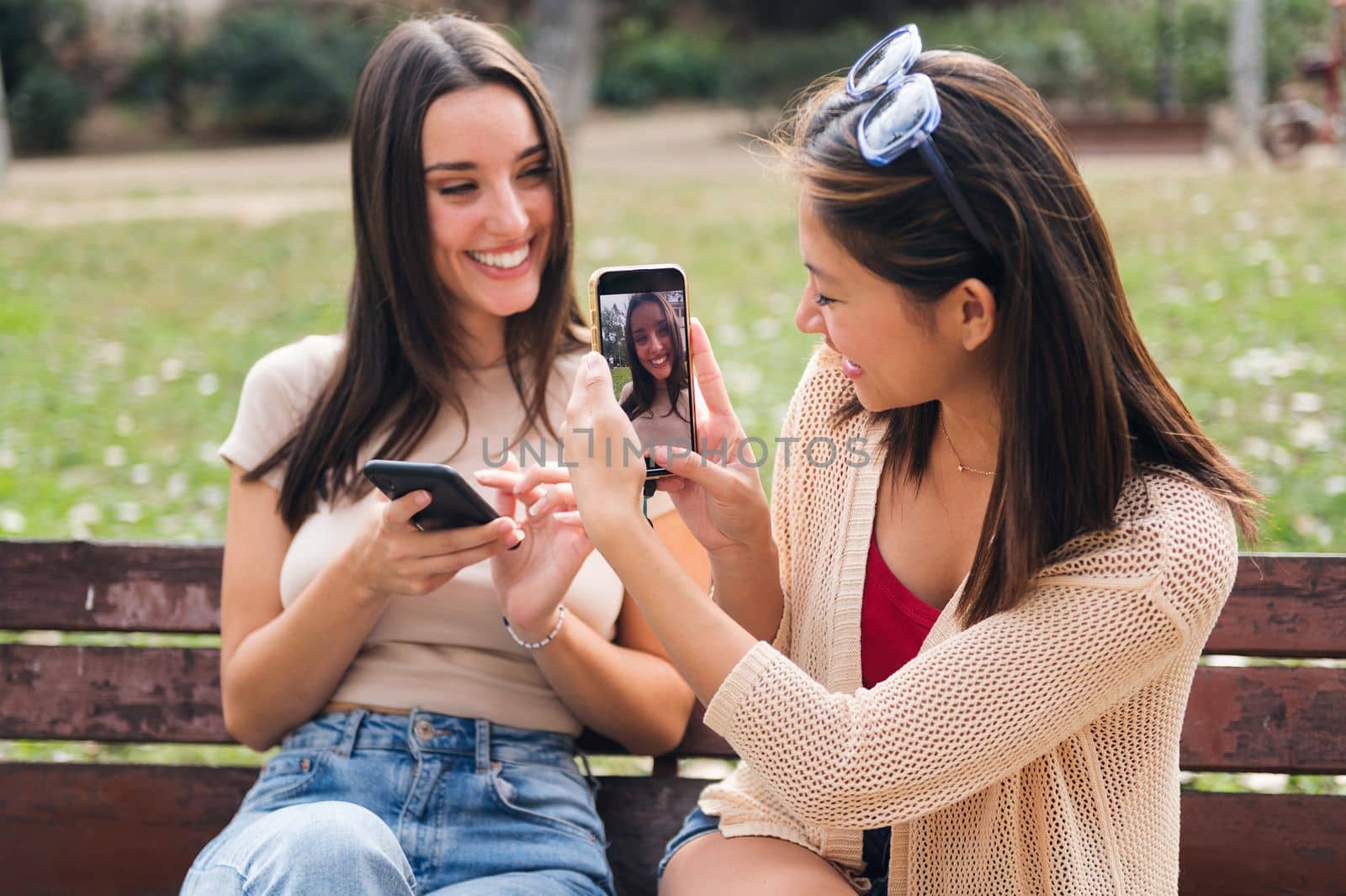 young woman taking a photo of her friend with a mobile phone, concept of technology of communication and teenager lifestyle