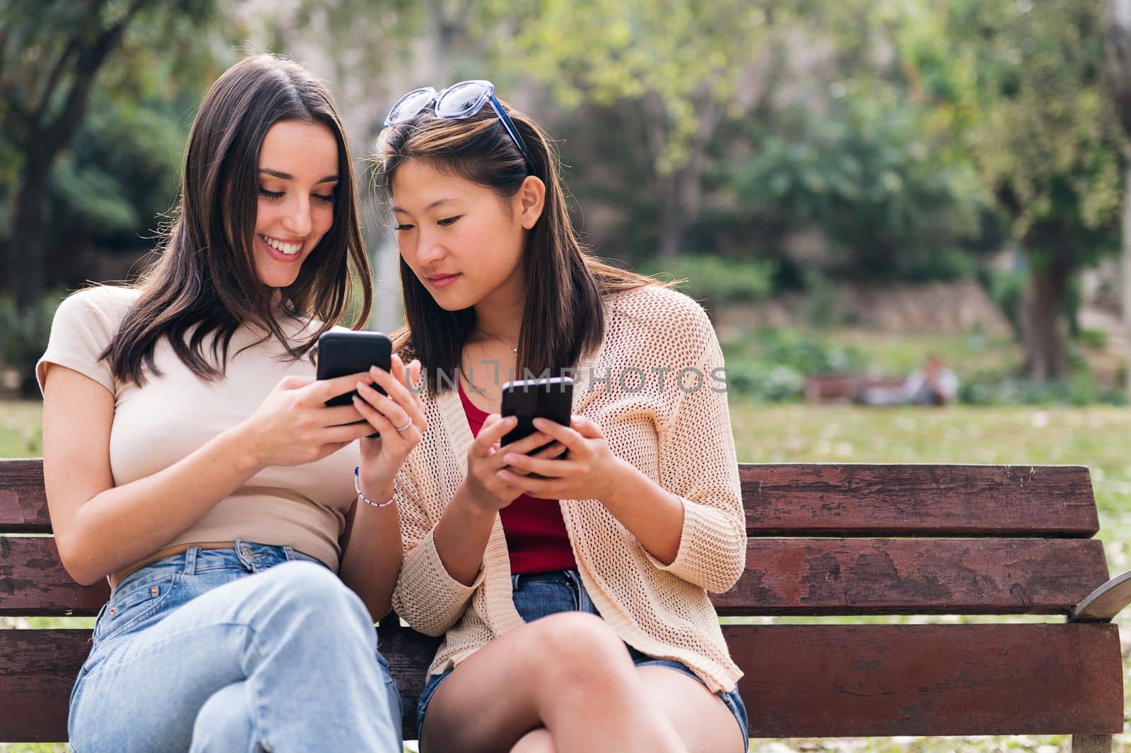 two young women smiling happy while looking their mobile phones, concept of youth and communication, copy space for text