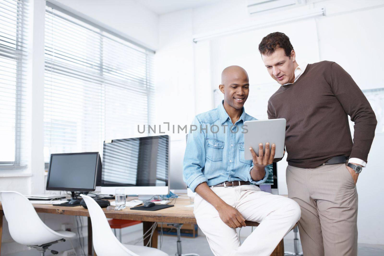 Using technology in the workplace. Two businessmen working on a digital tablet in the office. by YuriArcurs