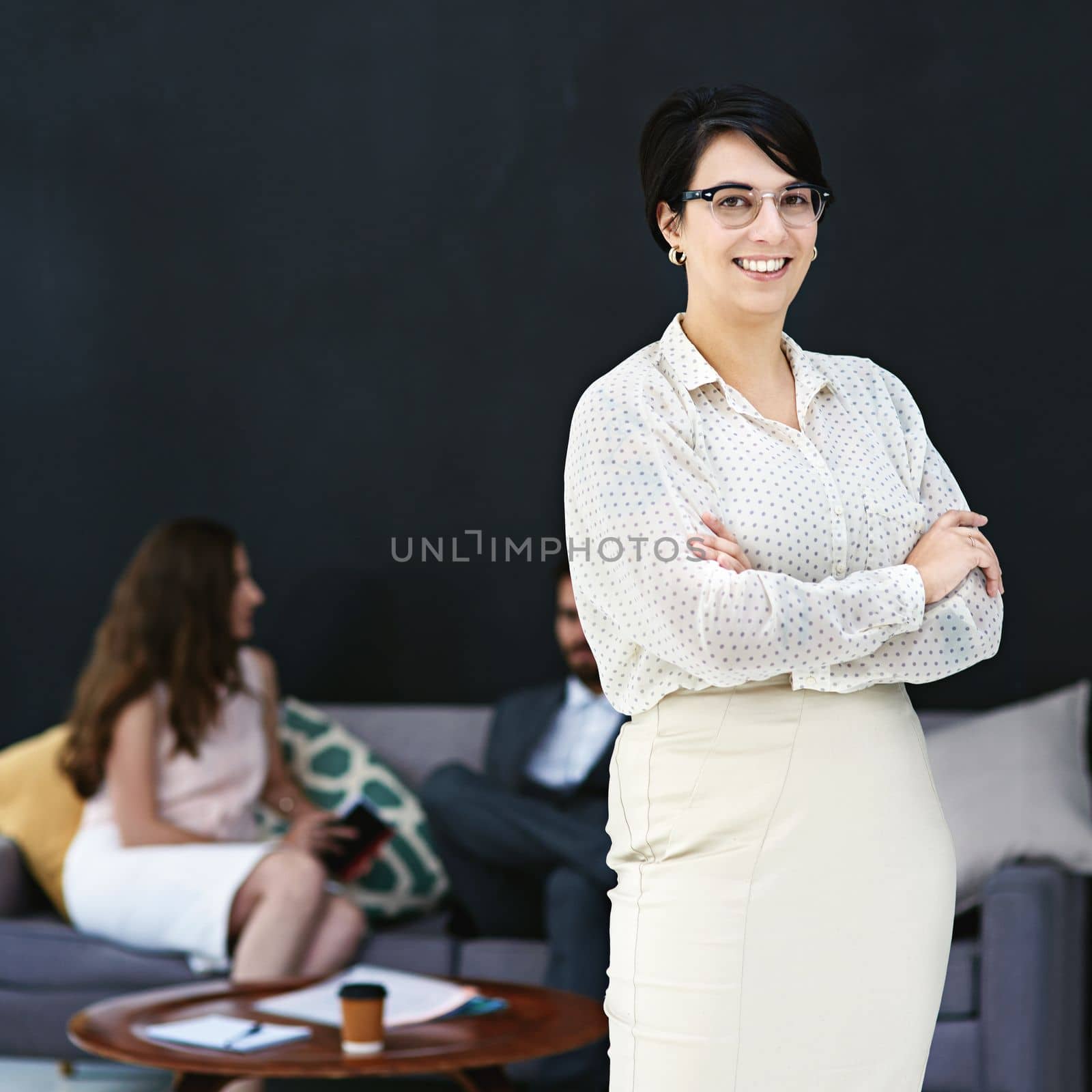 Im a part of the best in the business. Portrait of a young businesswoman standing in a modern office with colleagues in the background. by YuriArcurs