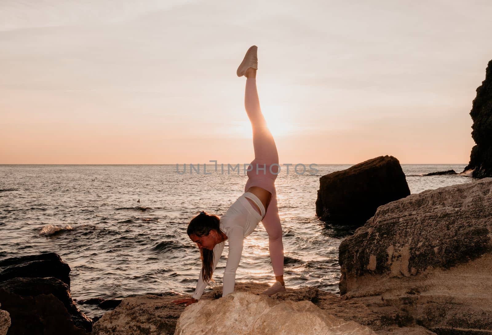 Young woman with black hair, fitness instructor in pink sports leggings and tops, doing pilates on yoga mat with magic pilates ring by the sea on the beach. Female fitness daily yoga concept