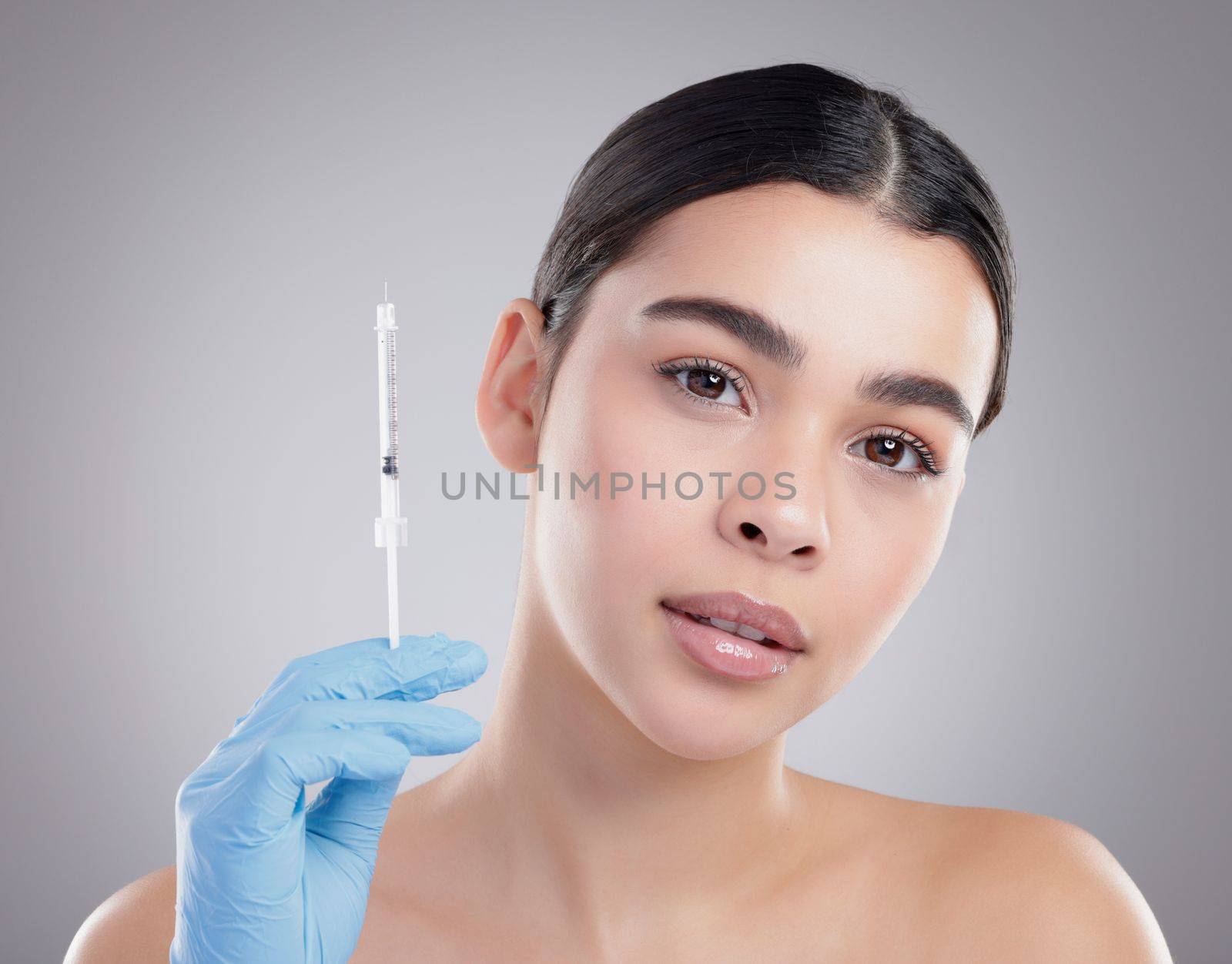 Botox beauty. Studio portrait of an attractive young woman holding a botox injection against a grey background. by YuriArcurs