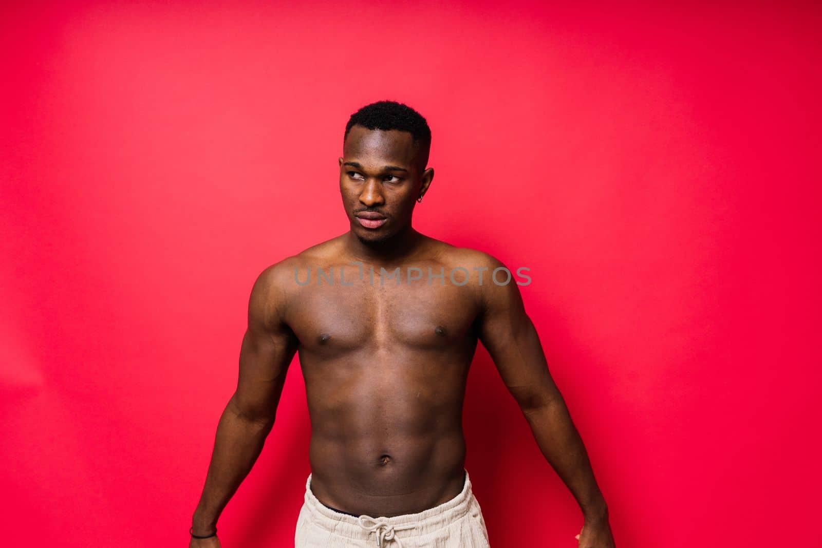 One young handsome african man topless portrait in studio on red background by Zelenin