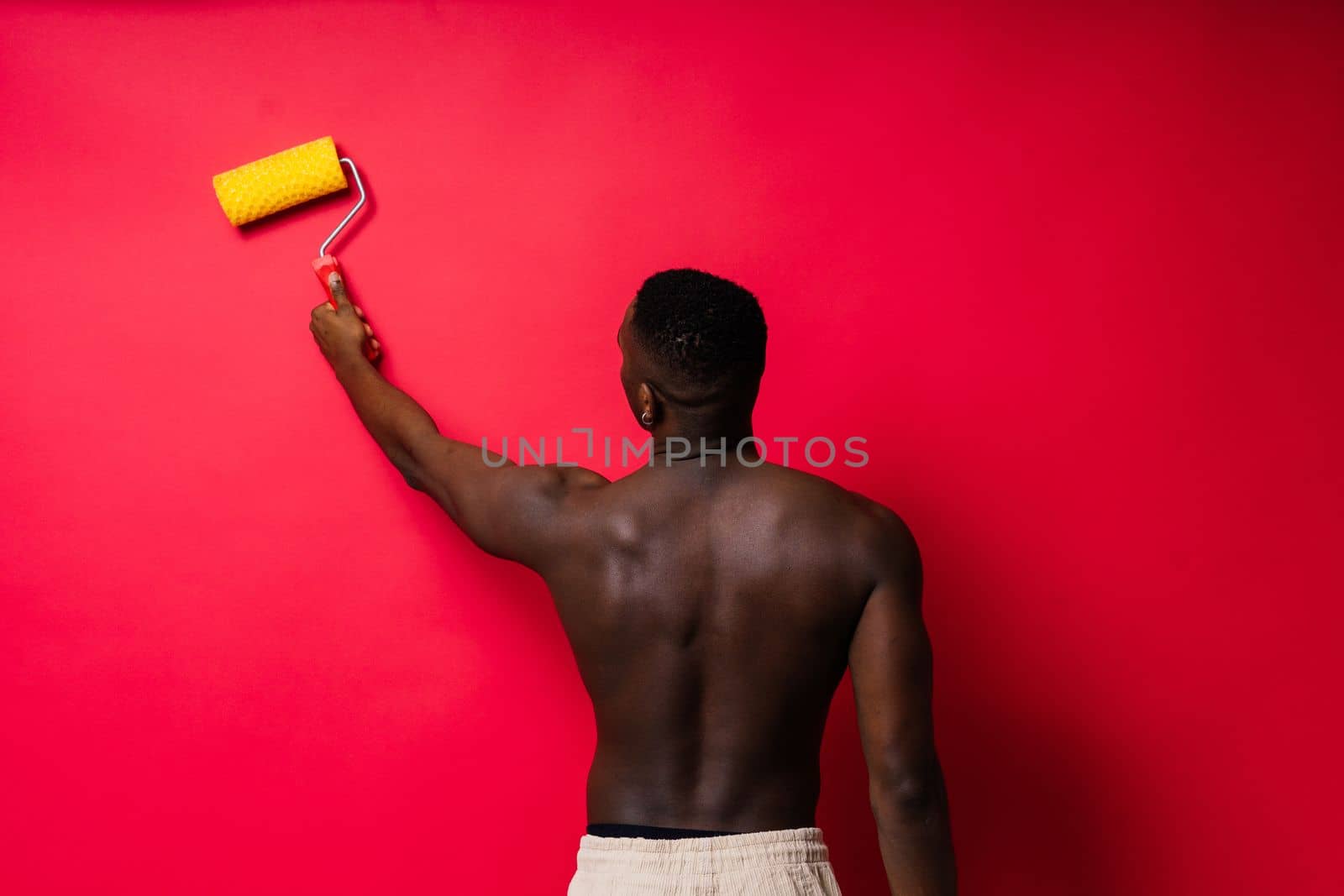 African painter focused on work holding professional roller to paint interior wall, studio.