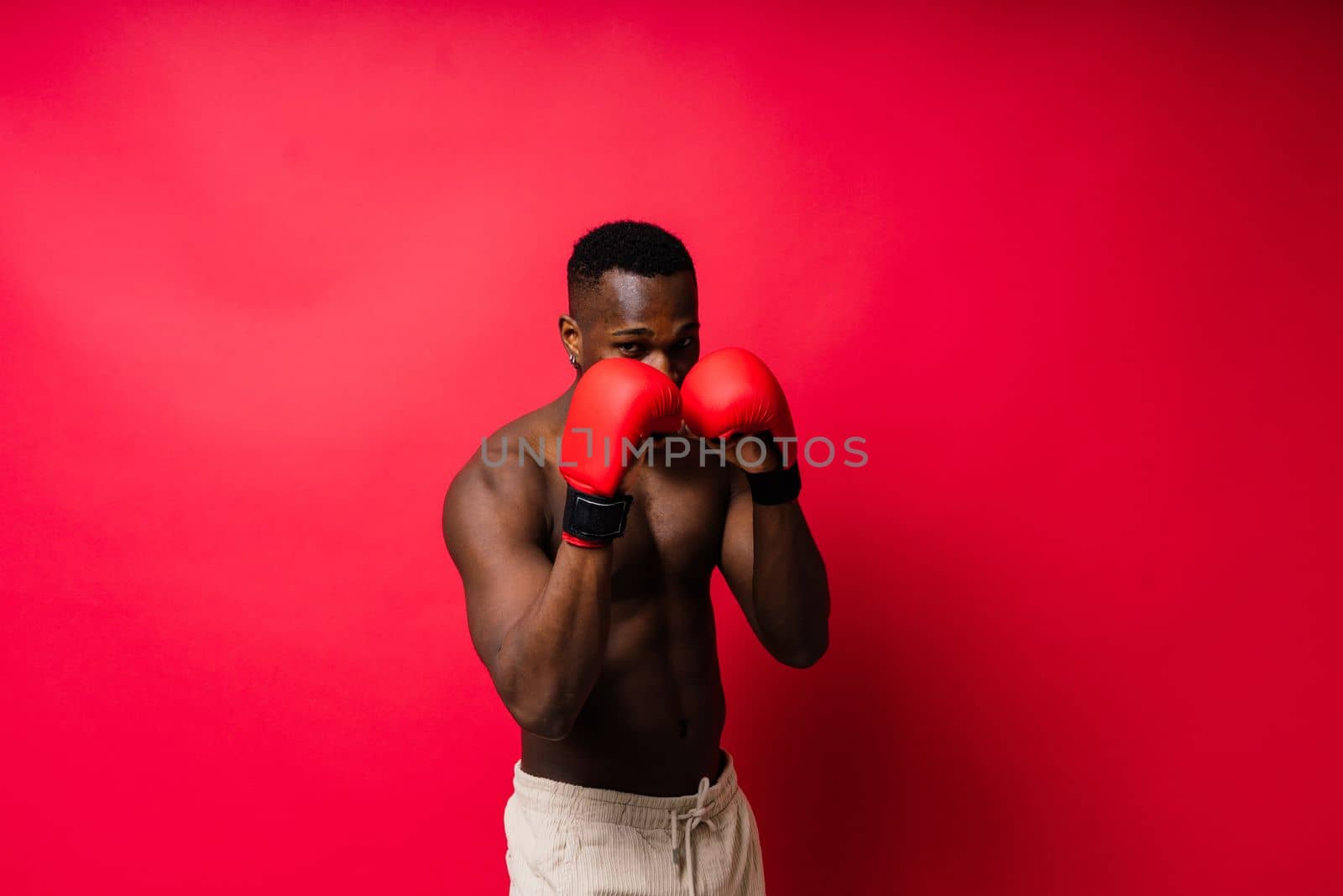 Muscular serious looking african boxer training, studio red background by Zelenin