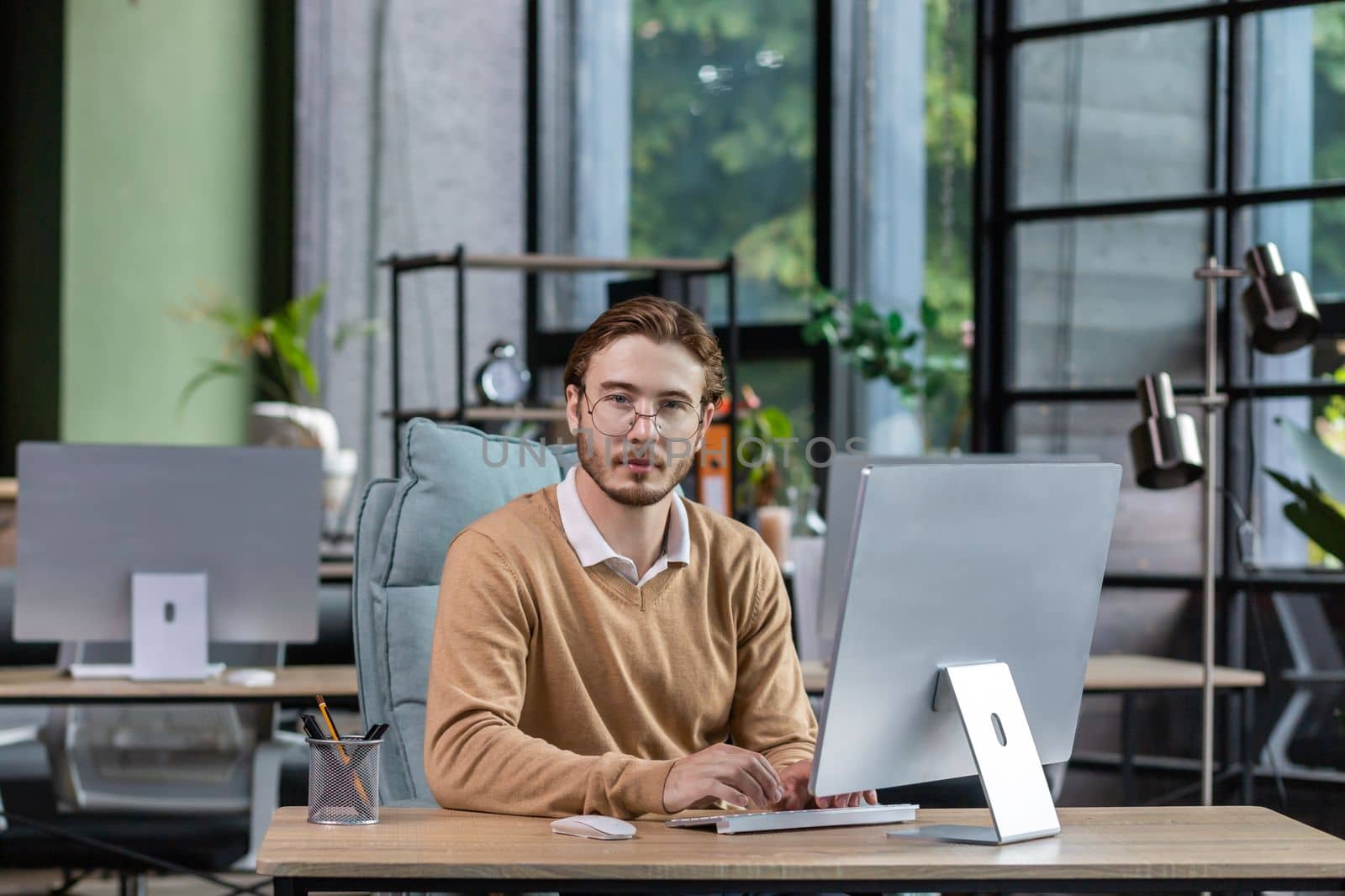Portrait of thinking serious man with computer inside modern green loft office, blond man looking thoughtfully at camera businessman in casual clothes working with computer by voronaman