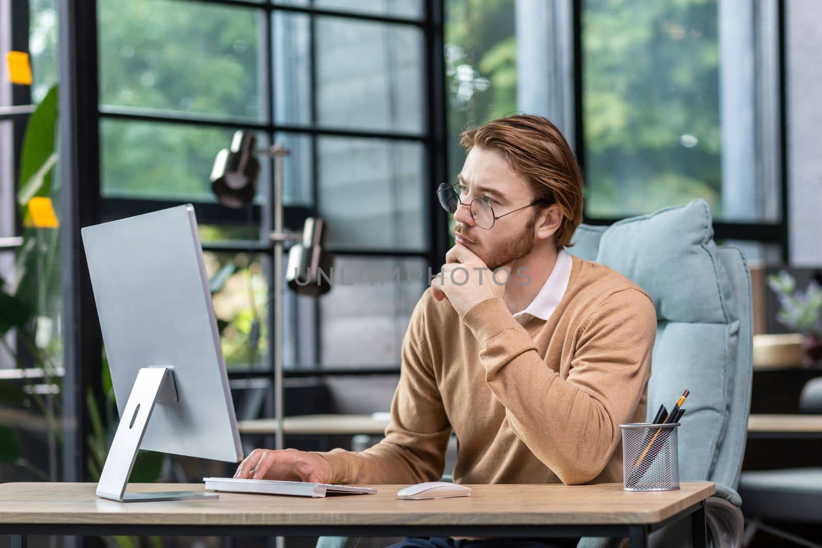 Thinking blond businessman at work inside modern green loft office, young man in casual clothes seriously ponders decision and completes task by voronaman
