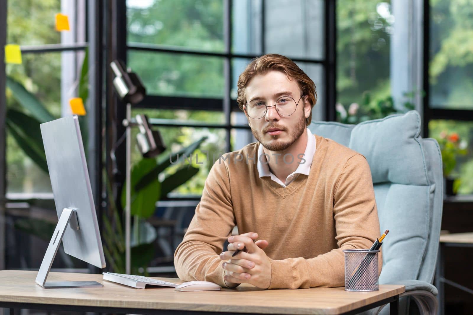 Portrait of thinking serious man with computer inside modern green loft office, blond man looking thoughtfully at camera businessman in casual clothes working with computer.