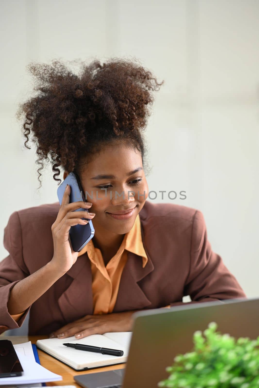 Smiling African American businesswoman in stylish suit having pleasant conversation while sitting at workstation.