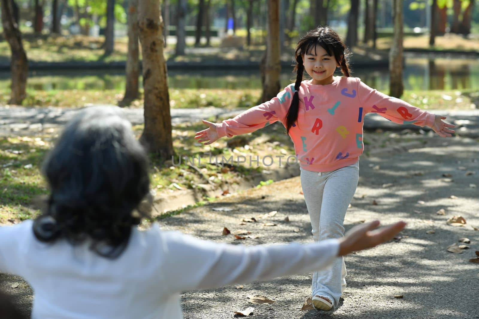 Loving grandmother stretching out arms to side while smiling grandchild running towards her in the park. Family and love concept.