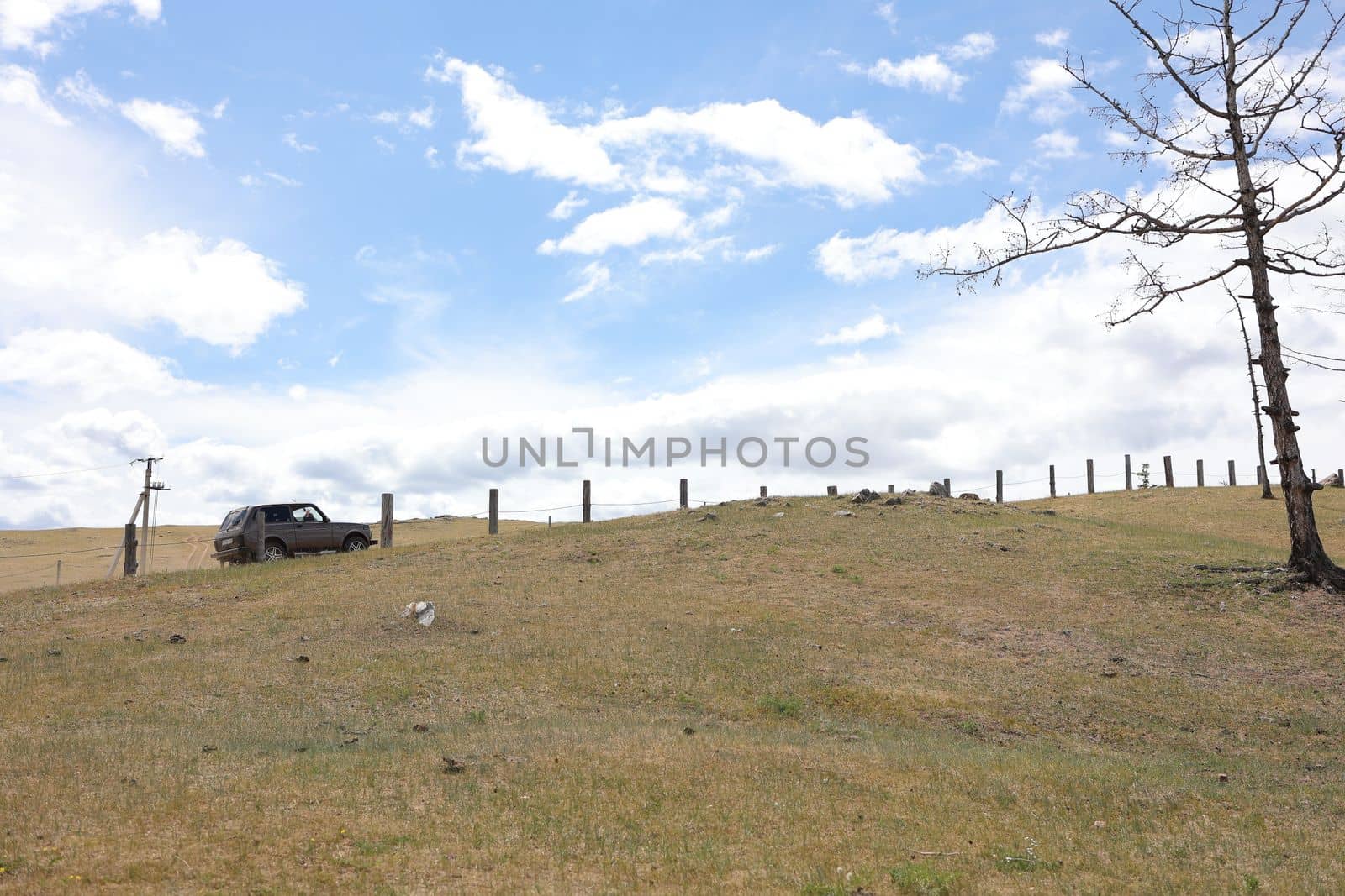 A car drives uphill on Olkhon Island along an old fence