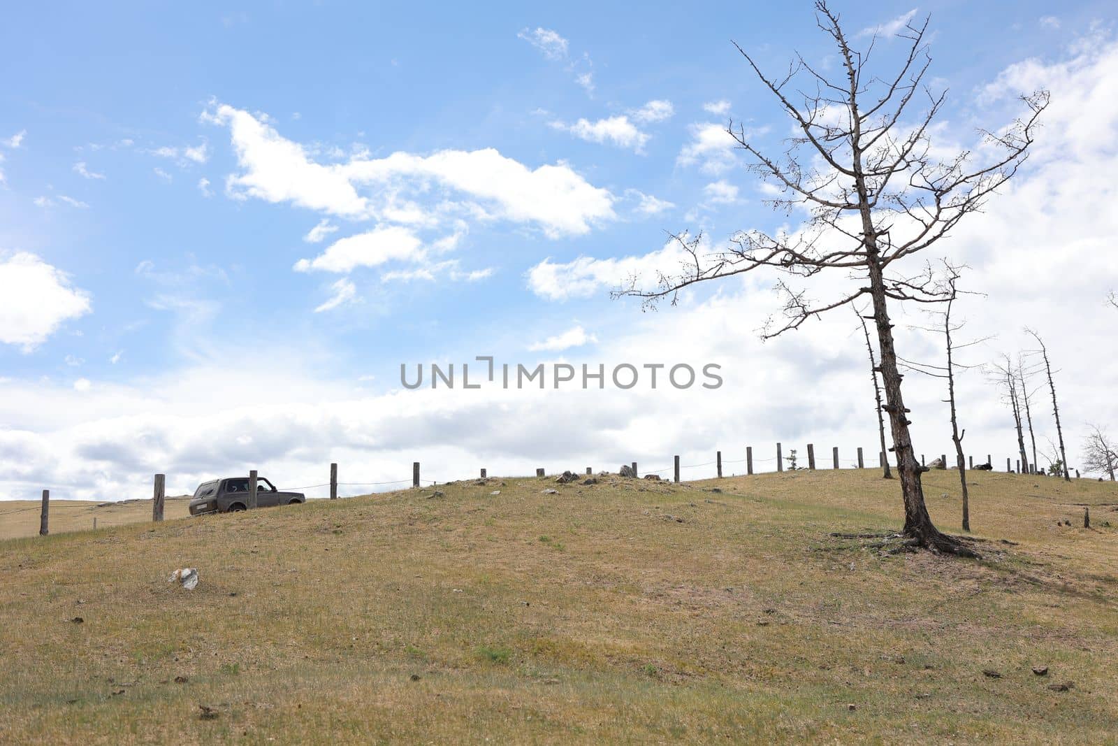 An off-road vehicle drives uphill along a Baikal road along a fence on Olkhon Island