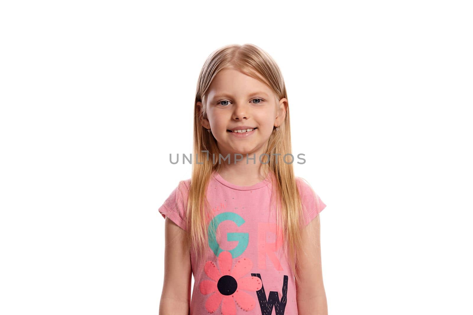 Close-up portrait of a cheerful blonde little female with a long hair, in a pink t-shirt, looking happy isolated on white background with copy space. Concept of a joyful childhood.