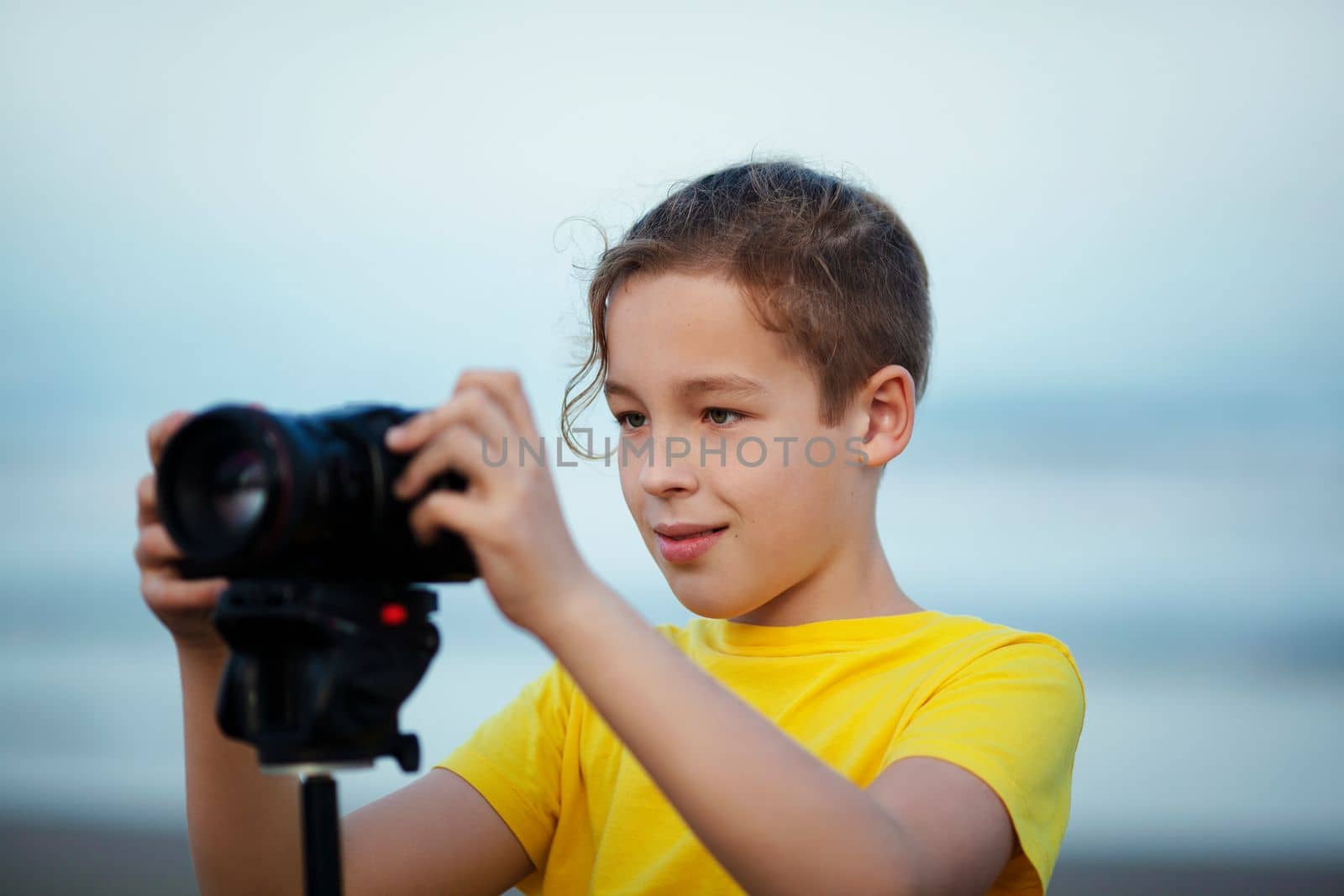 Boy teenager with digital camera on tripod outdoors. Child interested in photography-videography learning to take picture and make videos