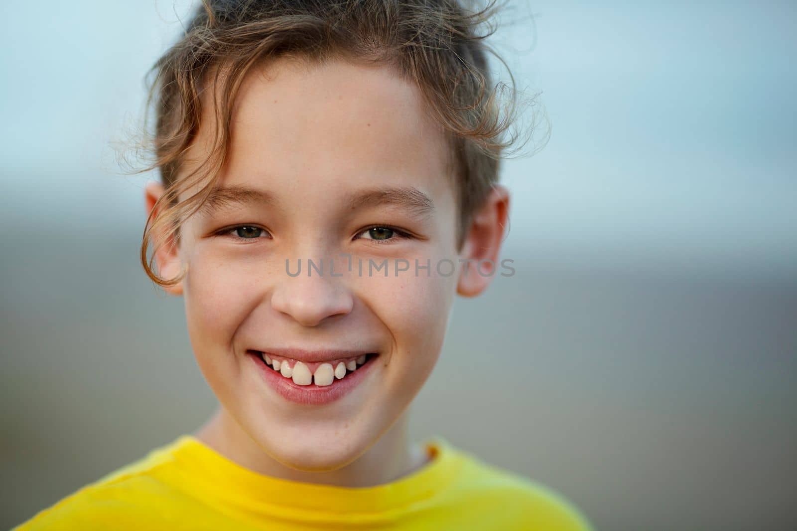 Close-up portrait of a cheerful boy with curly fair hair. Child with a big smile looking to the camera, blurry background