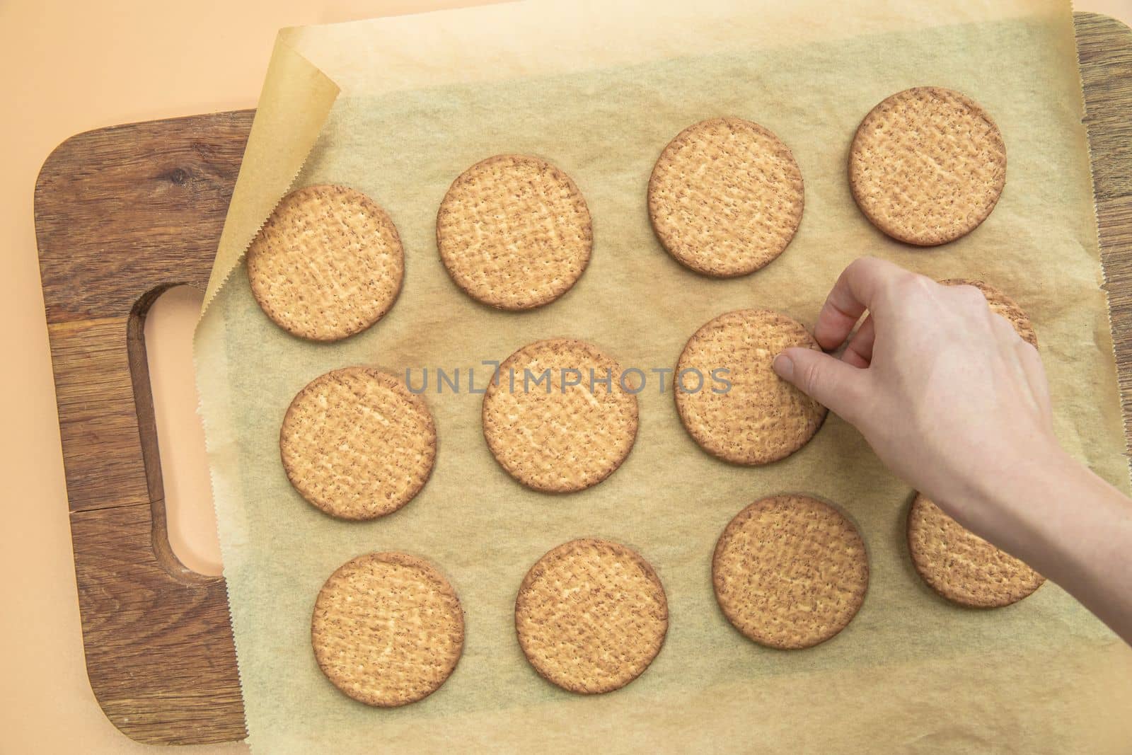 Woman hand taking freshly baked normal grain healthy cookie top view, on wooden plate