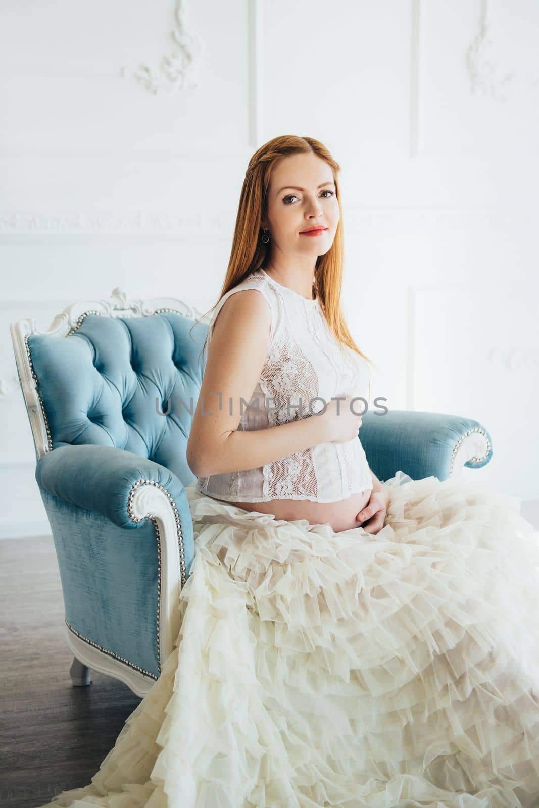 red-haired pregnant young girl in a blue armchair of a bright room
