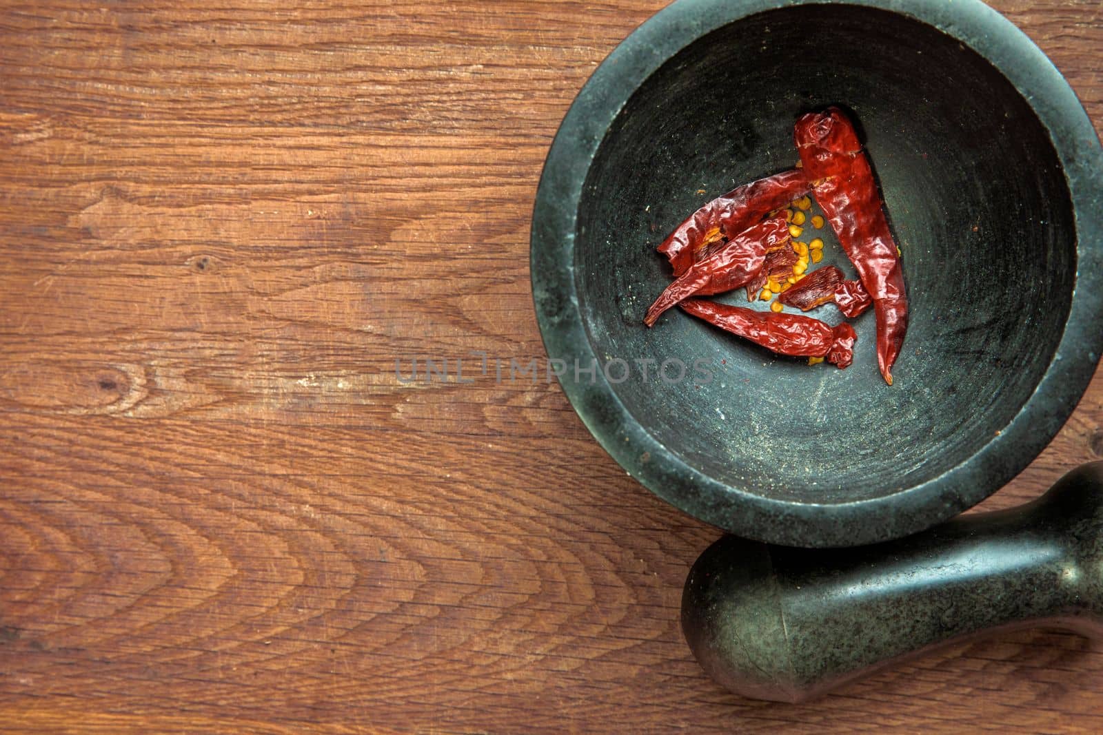 Red hot pepper in a stone granite mortar, dried chillies crunched top view on wooden background copy space healthy food
