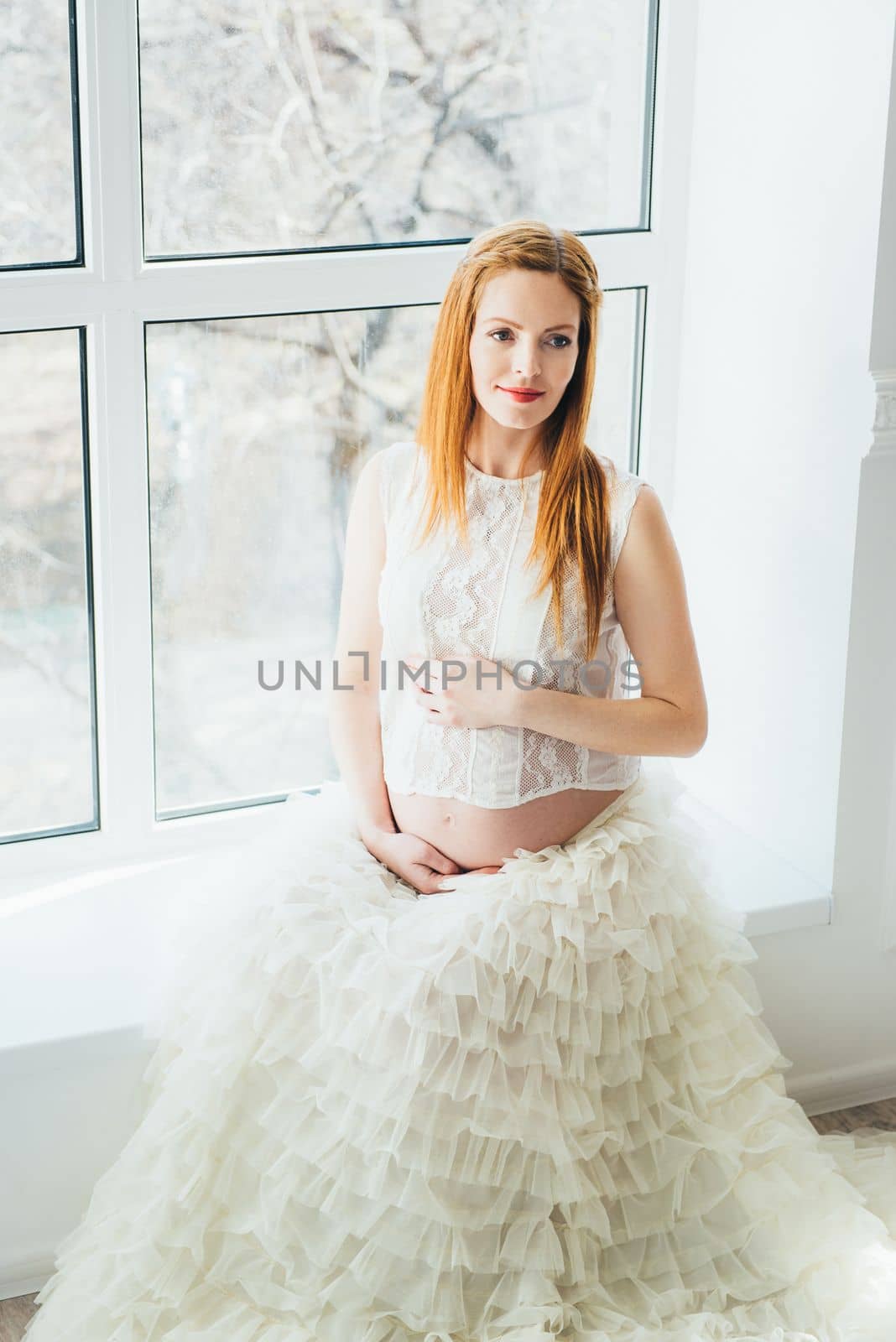 red-haired pregnant young girl in a white dress near the window by Andreua