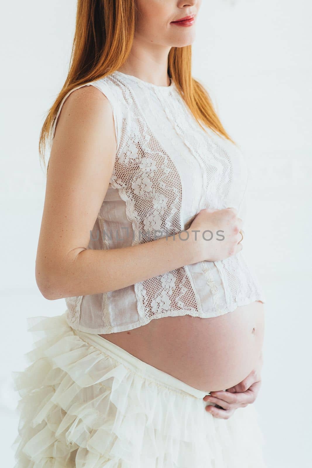 red-haired pregnant young girl in a white dress near the white wall by Andreua