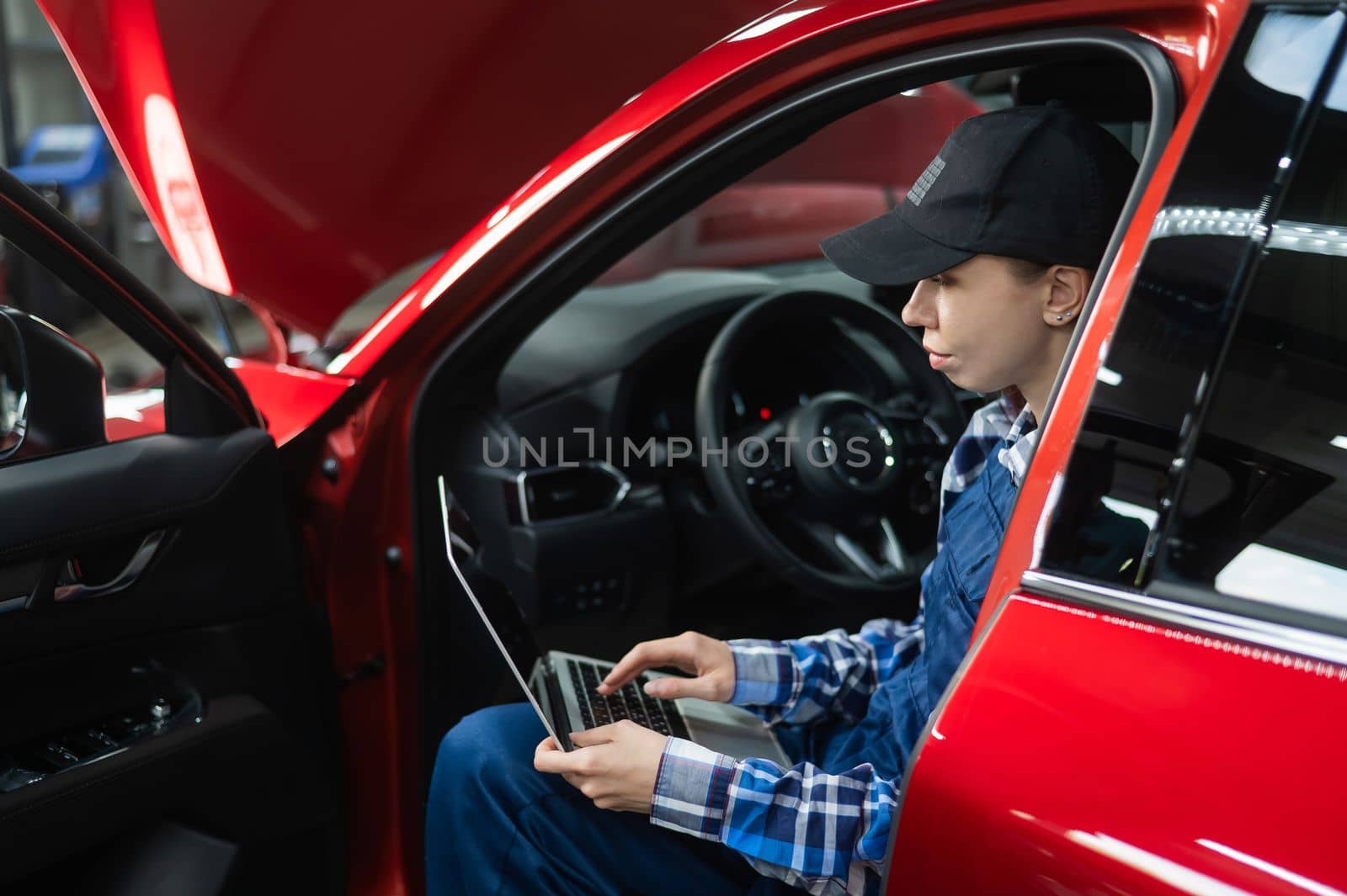 Woman auto mechanic doing diagnostics in car using laptop