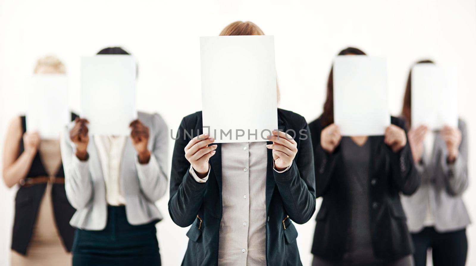 The reason behind their business success. a group of unrecognizable businesspeople holding blank pieces of paper over their faces against a white background. by YuriArcurs