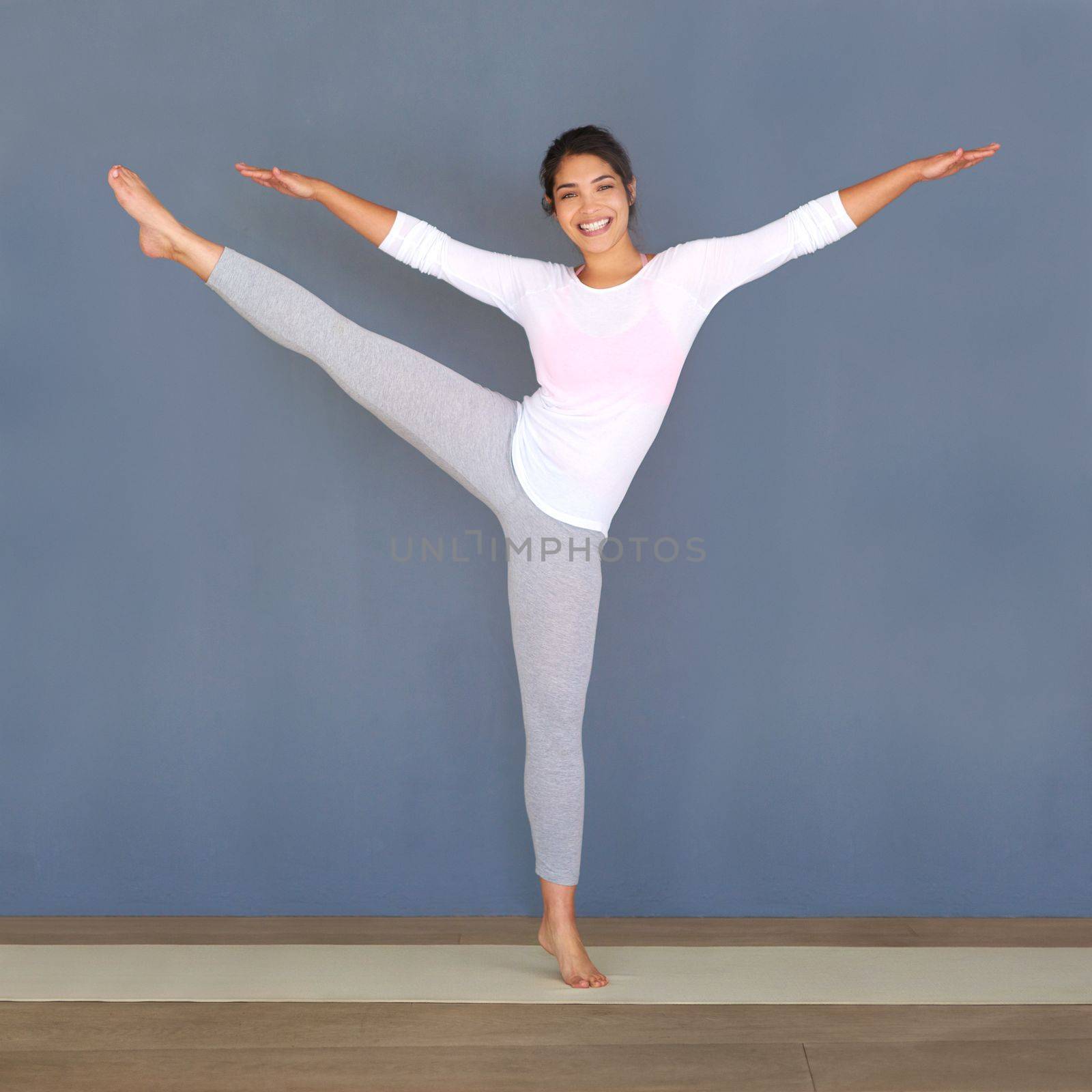 Stretching allows you to do much more while working out. Full length shot of a sporty young woman doing yoga against a grey background. by YuriArcurs