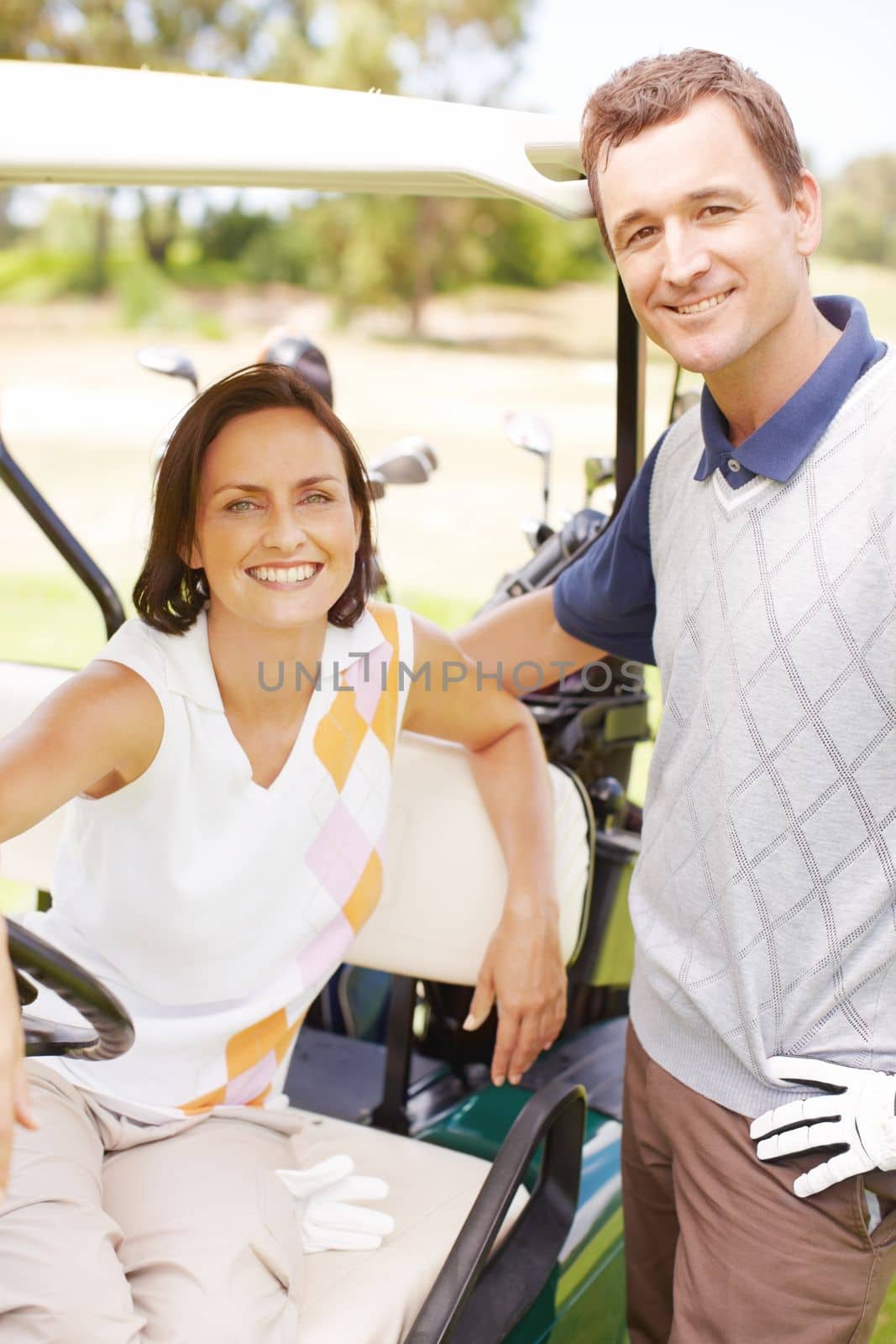 Their love of golf brought them together. Smiling woman seated in a golf cart with her husband standing alongside her