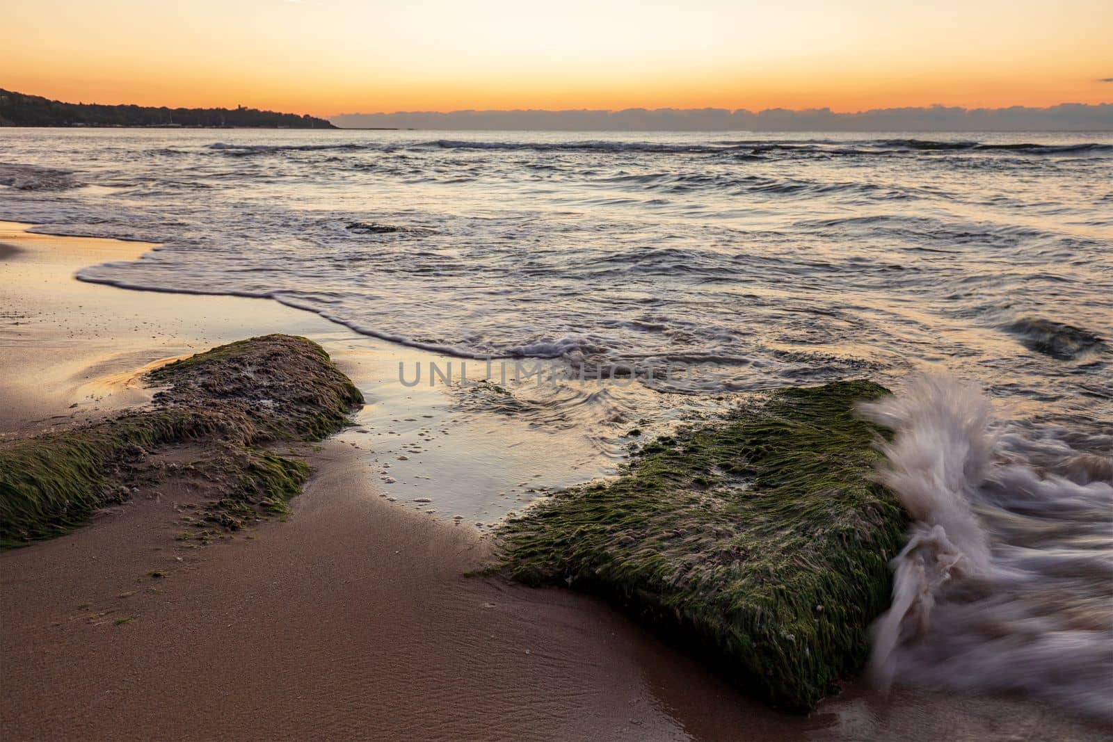 Seascape view with rocks with moss and small wave splash.