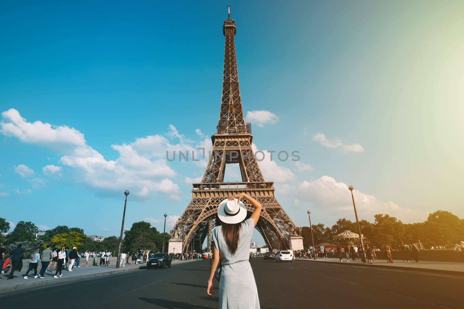 Rear view of woman tourist in sun hat standing in front of Eiffel Tower in Paris. Travel in France, tourism concept. Holiday or vacation in Paris by DariaKulkova