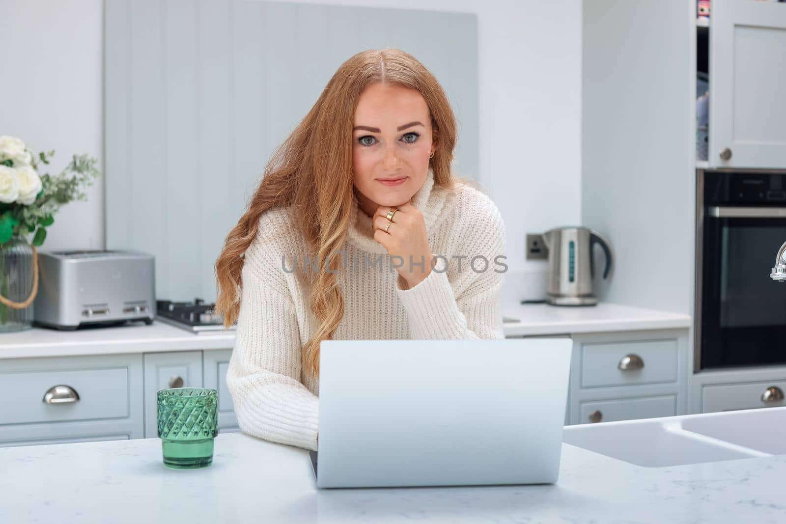 Beautiful middle age woman with laptop working from home online at her cozy kitchen by Len44ik