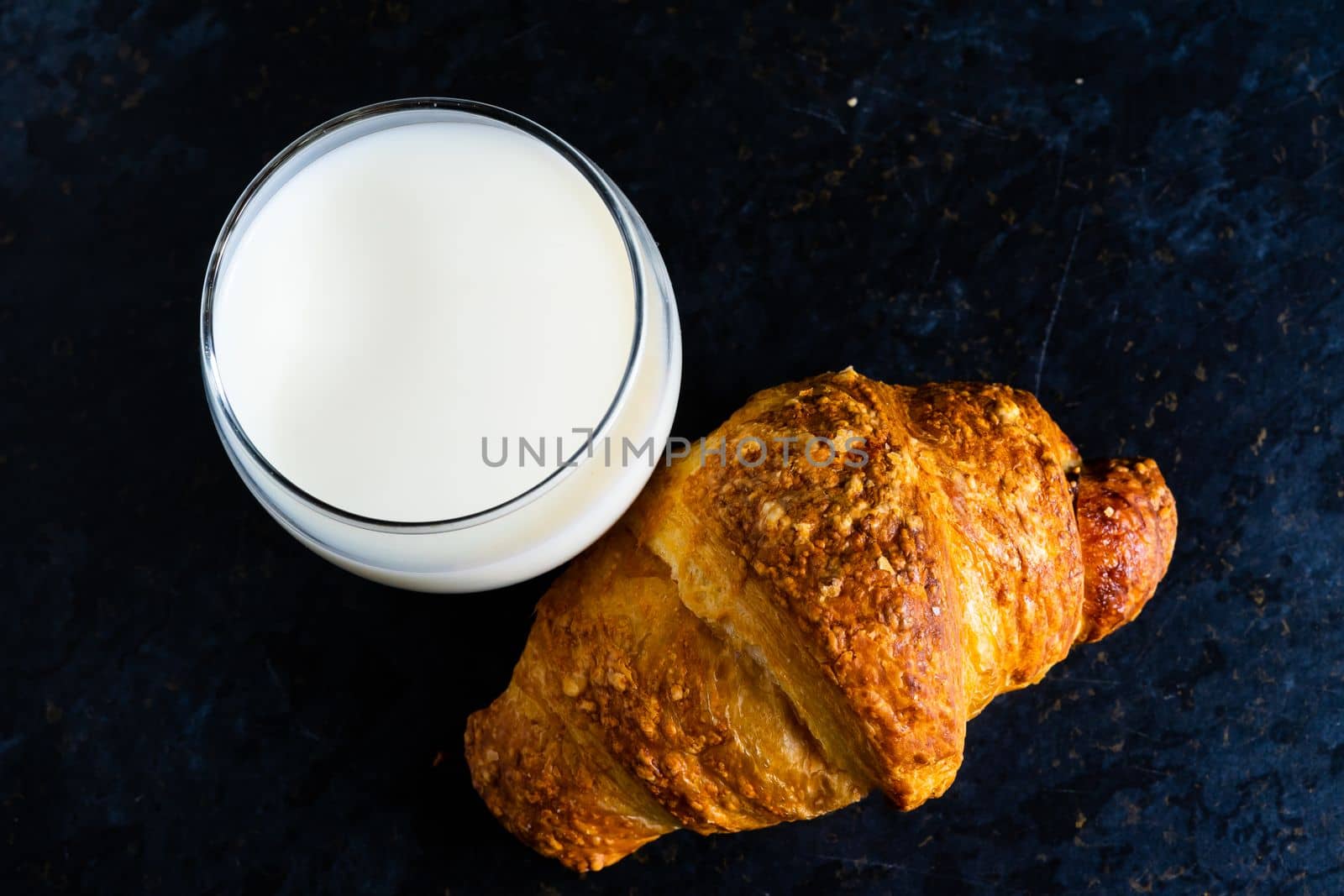 Fresh white bread and milk in white glass on a black stone table background. Top view, croissant